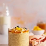 Creamy mango amaranth pudding topped with berries, coconut flakes, and maple syrup in glass jars.